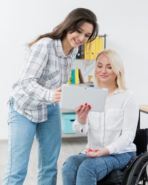A female occupational therapist is talking to a patient on a tablet, demonstrating range-of-motion exercises. The patient is positioned comfortably in a wheelchair.